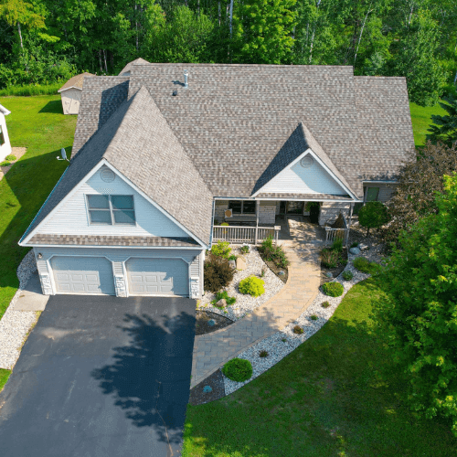 Aerial view of a residential home with a newly installed asphalt shingle roof, landscaped yard, and paved walkway, showcasing quality roofing services by Perrault Construction in Two Harbors, MN.