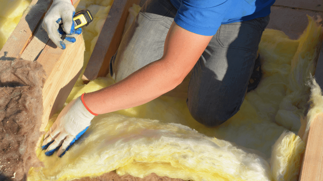 Person installing fiberglass insulation in attic, demonstrating insulation techniques for energy efficiency and comfort, relevant to Perrault Construction's services in Duluth, MN.