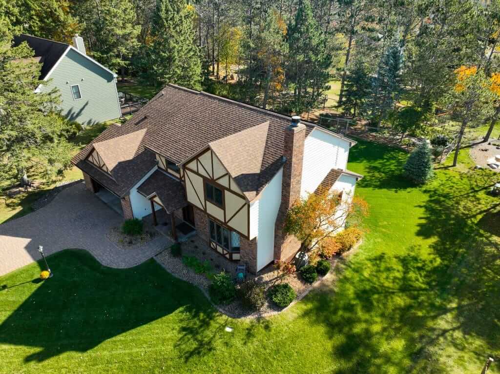 Aerial view of a residential home with a well-maintained roof, surrounded by lush greenery and trees, highlighting quality roofing services in Two Harbors, MN.