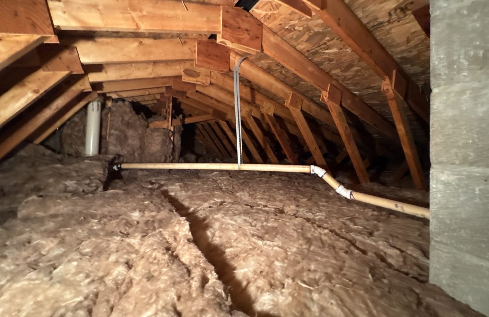 Attic with thin, uneven fiberglass insulation between the ceiling joists