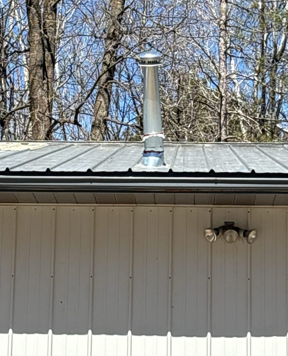 Close-up of a metal vent pipe rising through a roof above a building wall