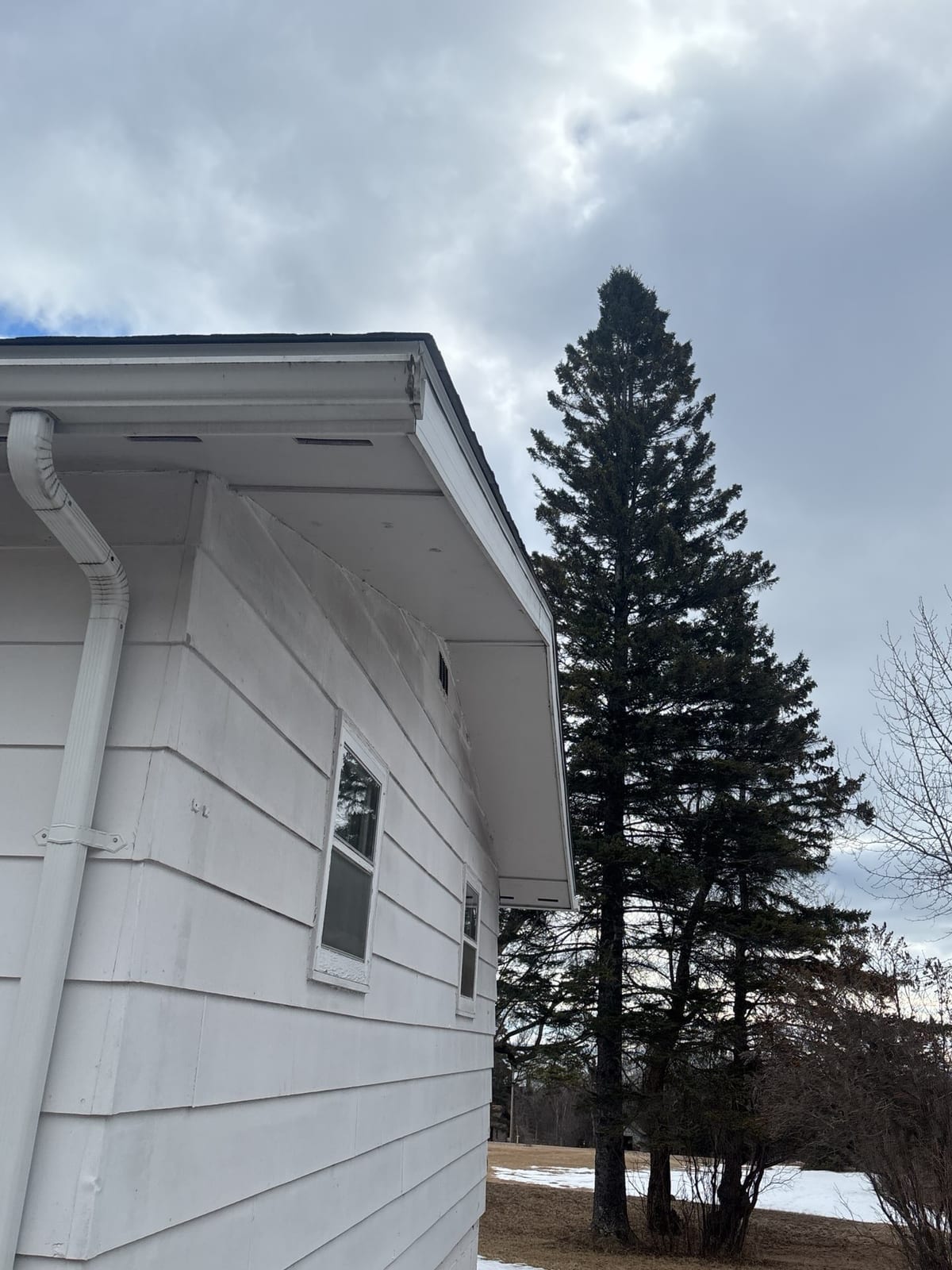 White house corner with new roof edge, gutter and downspout under a cloudy sky